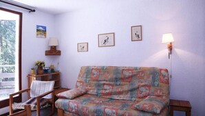 Um quarto acolhedor com um sofá, uma cadeira, uma mesinha com abajur e quadros nas paredes.