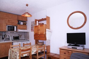 A compact kitchen with wooden cabinets, a microwave, a stove, and a dining table with chairs.