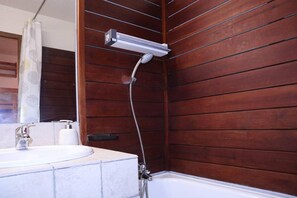 A bathroom with a wooden panel wall, a white sink, and a shower with a handheld showerhead.