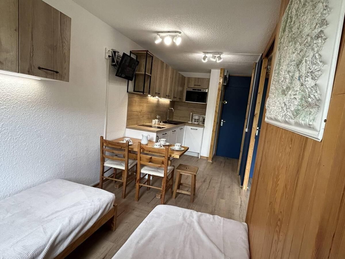 A compact room with two single beds, a wooden dining table with chairs, a kitchenette, and a small bathroom.