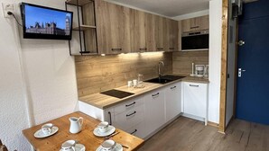 Una cocina compacta con armarios de madera, un lavamanos integrado y una zona de comedor con una mesa preparada para cuatro.