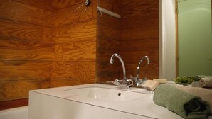 Un baño con pared de madera, un lavamanos blanco, dos grifos, una toalla y una planta pequeña.