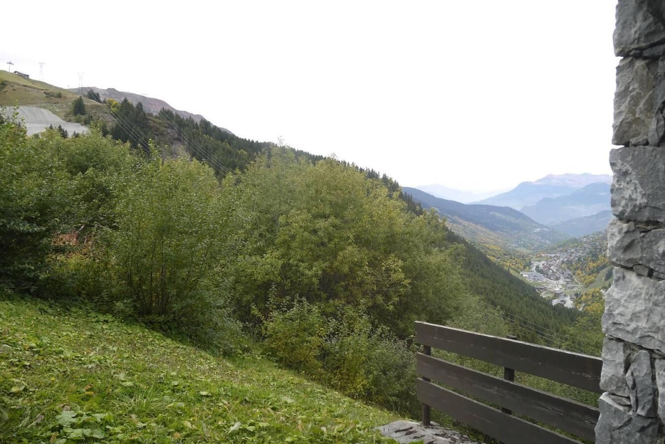 Eine Bank mit Blick auf ein Tal, üppigem Grün und ferne Berge.