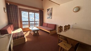 A cozy room with a wooden table, two sofas, a small table, and a window with curtains. - 150m from shops, 5th floor, view ski slopes, balcony, ski locker, 60m², Méribel-Mottaret (Méribel - Les Allues)