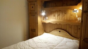 A wooden-framed bed with a white quilt, two wall-mounted lights, and a small shelf above the bed. - 150m from shops, 5th floor, view ski slopes, balcony, ski locker, 60m², Méribel-Mottaret (Méribel - Les Allues)