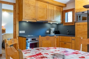 Una cucina compatta con mobili in legno, un fornello, una moka e un tavolo con tovaglia a quadretti rossi e bianchi.