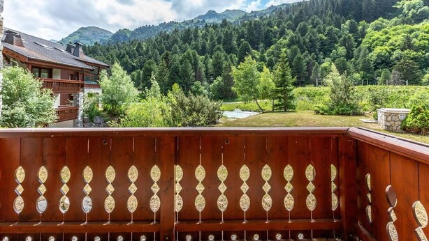 A wooden deck with a view of a mountainous landscape and a building with a sloped roof.
