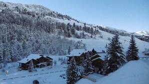 A snow-covered lodge with multiple wooden cabins, surrounded by snow-laden trees and mountains.