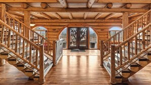 A wooden interior with a central staircase, wooden railings, and a view through an arched doorway.