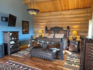A bedroom with a wooden ceiling, a bed with a headboard, bedside tables, a dresser, and a rug. - Expansive Lodge on 80 Acres! Hot Tub, Decks, WiFi! (Florissant)