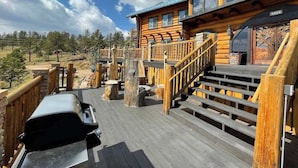 A wooden deck with a barbecue grill, wooden stairs, and a view of a forested area.