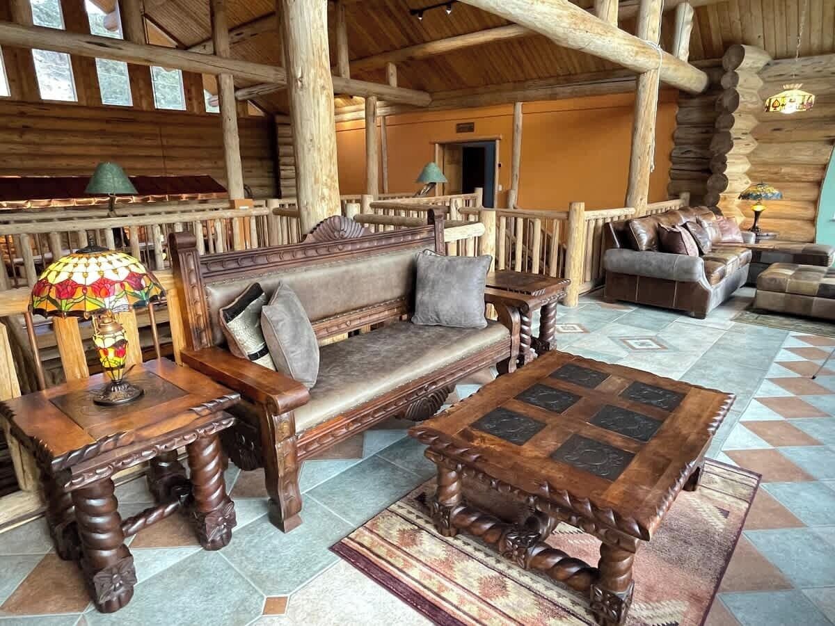 A log cabin interior with a wooden sofa, a coffee table, and a lamp.