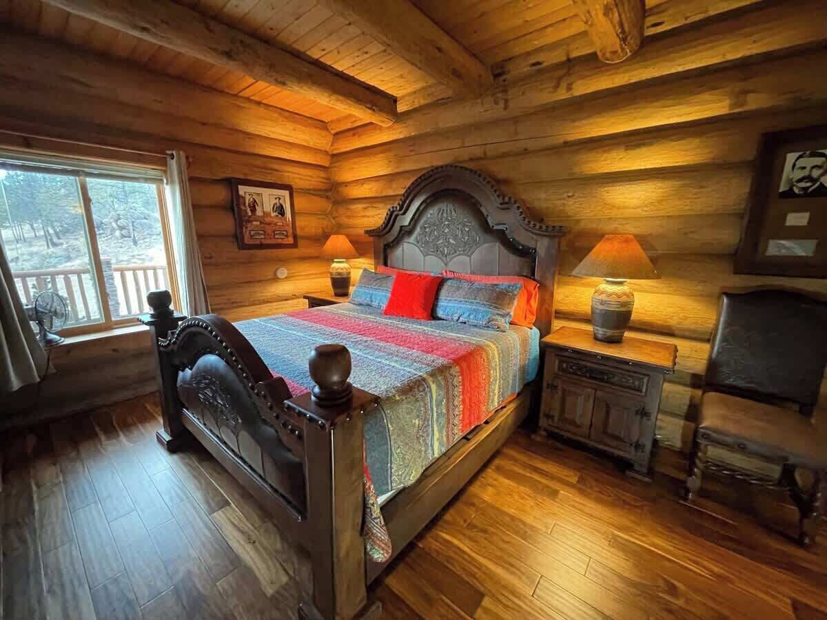 A wooden cabin bedroom with a bed, two bedside tables, a chair, and a window.