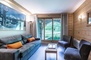 A cozy room with a sofa, armchair, and a table. There is a large window with curtains, and a painting on the wall. - 80m from ski lifts, view ski slopes, terrace, ski locker, 43m², Méribel-Mottaret (Méribel - Les Allues)