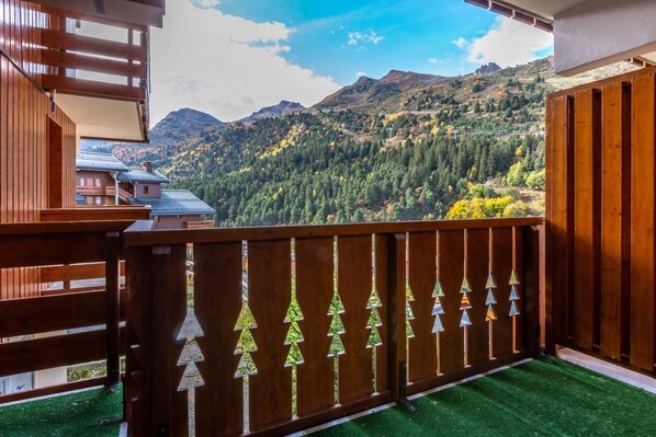 A balcony with a view of a mountainous landscape, a wooden fence with tree-shaped cutouts, and artificial green grass.