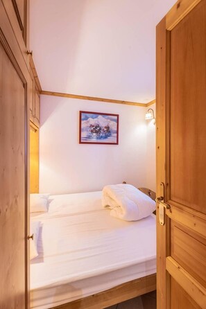 Quarto com cama, porta de madeira, luminária na parede e quadro emoldurado.