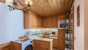 A compact kitchen with wooden cabinets, a washing machine, a microwave, and a small dining area.