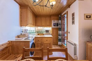 Uma cozinha compacta com armários de madeira, máquina de lavar e sala de jantar com cadeiras.