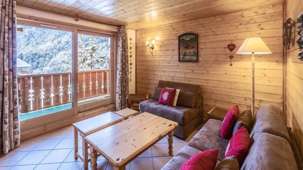 A wooden interior with a sofa, a table, and a window with a view of snow-covered trees.