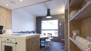 Una cocina compacta con horno integrado, un comedor con mesa y sillas, y un amplio ventanal con vistas a un paisaje nevado.
