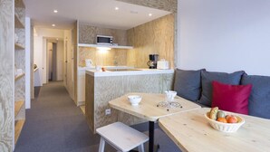 Un espacio habitable compacto con kitchenette, comedor y zona de estar con sofá y cojines.