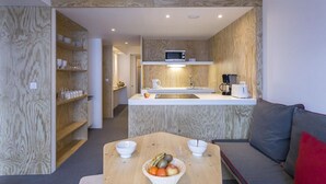 Cocina compacta con microondas, cafetera y lavamanos. Hay un comedor con mesa y sillas, además de un sofá con un cojín rojo.