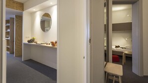 Una habitación de hotel moderna con diseño minimalista, que presenta un espejo grande, un escritorio pequeño con lámpara y un rincón de descanso acogedor.