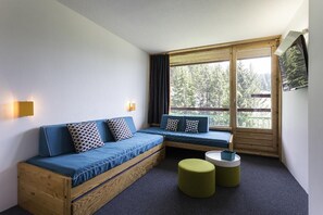 Een moderne kamer met een houten bank, een kleine ronde tafel en een aan de muur bevestigde televisie.