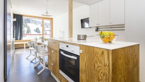 Une cuisine moderne avec un îlot central en bois, des meubles blancs et une grande fenêtre donnant sur un paysage enneigé.