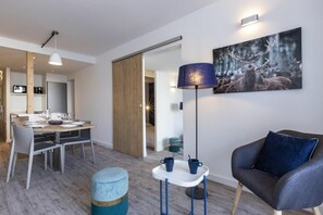 Uma sala de estar moderna com um sofá cinza, uma área de jantar com mesa posta para quatro pessoas e uma grande pintura de veados fixada na parede.
