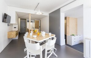 Una cocina moderna con una mesa de madera y sillas blancas, un horno empotrado y una pequeña isla con un lavaplatos.
