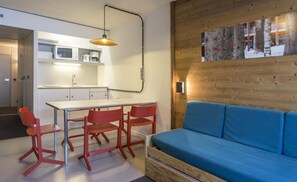 A compact living space with a kitchenette, a dining area with red chairs, a blue sofa, and a wooden accent wall with a framed picture. - 100m from resort center, 15th floor, balcony, tv, 27m², Les Arcs (Les Arcs)