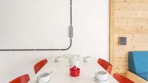 Una mesa blanca con sillas rojas, una tetera blanca y un exprimidor rojo.