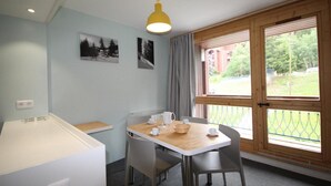A small room with a table set for two, a window with a view of greenery, and a yellow pendant light.