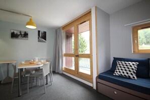 Quarto com mesa de jantar, cadeiras, sofá e janela com vista para árvores.