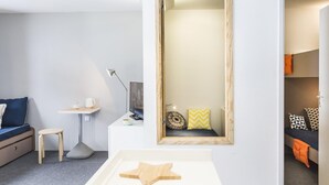 A modern, well-lit room with a bed, a small desk, a chair, and a mirror.