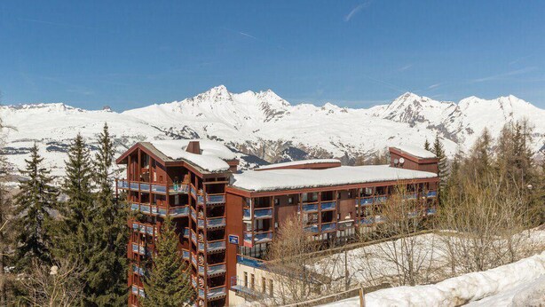 A multi-story hotel with balconies and a snow-covered mountain backdrop.