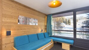 A wooden interior with a blue sofa, a wall-mounted light fixture, and a window with a view of a snowy landscape. - 100m from resort center, 8th floor, balcony, tv, 27m², Les Arcs (Les Arcs)
