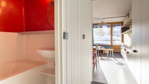 A modern kitchen with white cabinets, a red accent wall, and a view of the outdoors through large windows. - 100m from resort center, 8th floor, balcony, tv, 27m², Les Arcs (Les Arcs)