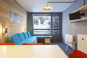 Une pièce moderne avec un mur en bois, un canapé bleu, un banc, une table, une chaise, un téléviseur et une fenêtre donnant sur un paysage enneigé.