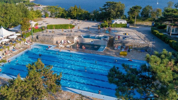 Une piscine dotée de plusieurs couloirs, entourée d’une terrasse en pierre et de parasols, et offrant une vue imprenable sur la côte, la mer et les collines lointaines.