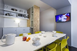 Une cuisine moderne avec un coin repas, des meubles blancs, un four à micro-ondes et un téléviseur fixé au mur.