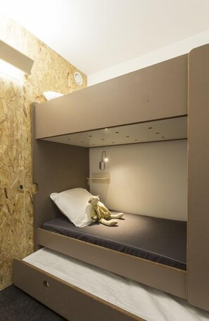 Un lit superposé avec un tiroir coulissant, une table de chevet avec une lampe et une étagère fixée au mur.