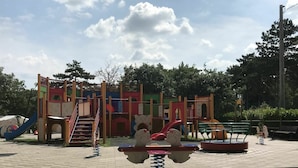 Ein Spielplatz mit verschiedenen Spielgeräten, darunter Rutschen und Kletterbereichen, unter einem Ziegeldach.
