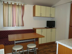 A compact kitchen with a wooden table, two stools, and a television on a cabinet.