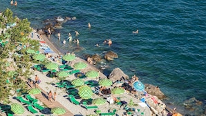 A beach with multiple green and white striped umbrellas, sun loungers, and people swimming and relaxing.
