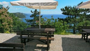 A picnic table with a white umbrella, set against a scenic backdrop of a coastal view with trees and hills.