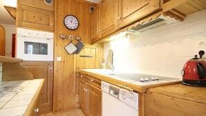 Una cocina compacta con armarios de madera, un reloj, una tetera y un lavavajillas.