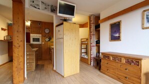 Una cocina compacta con armarios de madera, horno empotrado, refrigerador y televisor montado en la pared.