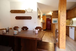 A dining area with a wooden table and chairs, a kitchen with wooden cabinets and appliances, and a red door leading to another room. - 50m from resort center, 4th floor, balcony, tv, 50m², Les Arcs (Les Arcs)
